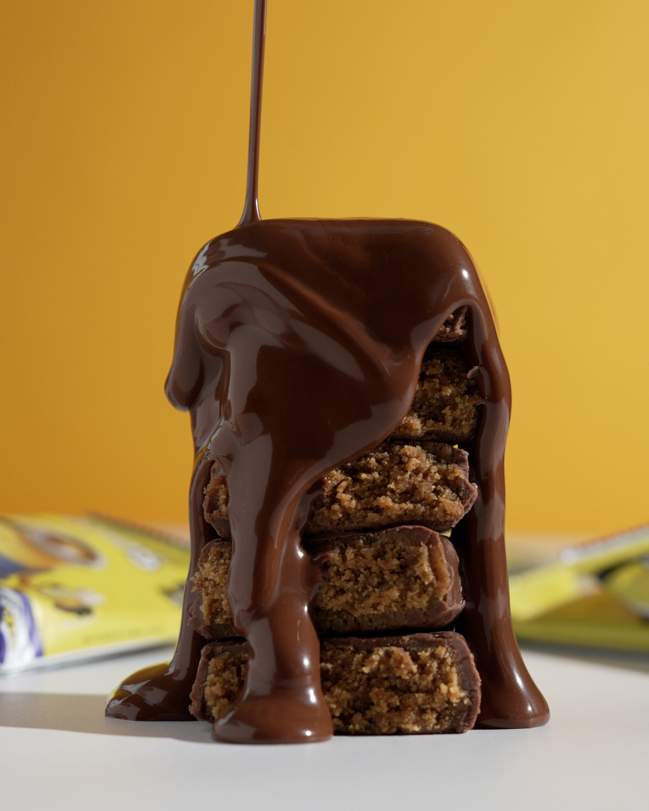 Trubar Banana Bread bars stacked under a chocolate pour against a yellow background